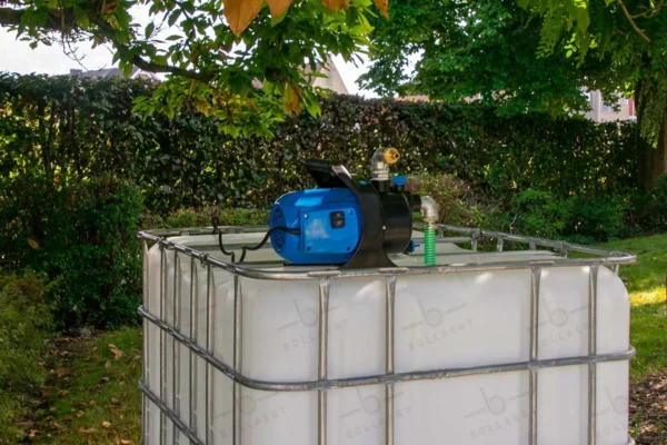 cuve-ibc-blanc-avec-pompe-220V-1000L-nettoye-palette-acier-plastique-vue-de-gauche-devant-dans-environnement-de-jardin.webp