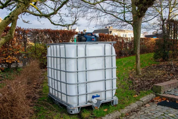 cuve-ibc-blanc-pompe-sur-batterie-1000L-nettoye-palette-acier-plastique-vue-de-gauche-environnement-du-jardin-sans-tuyau.webp